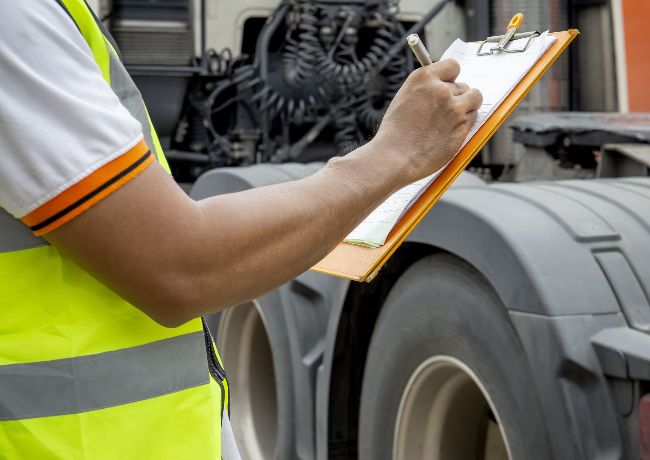 Personne en train de remplir un document papier devant des roues d'un camion (partie tracteur)